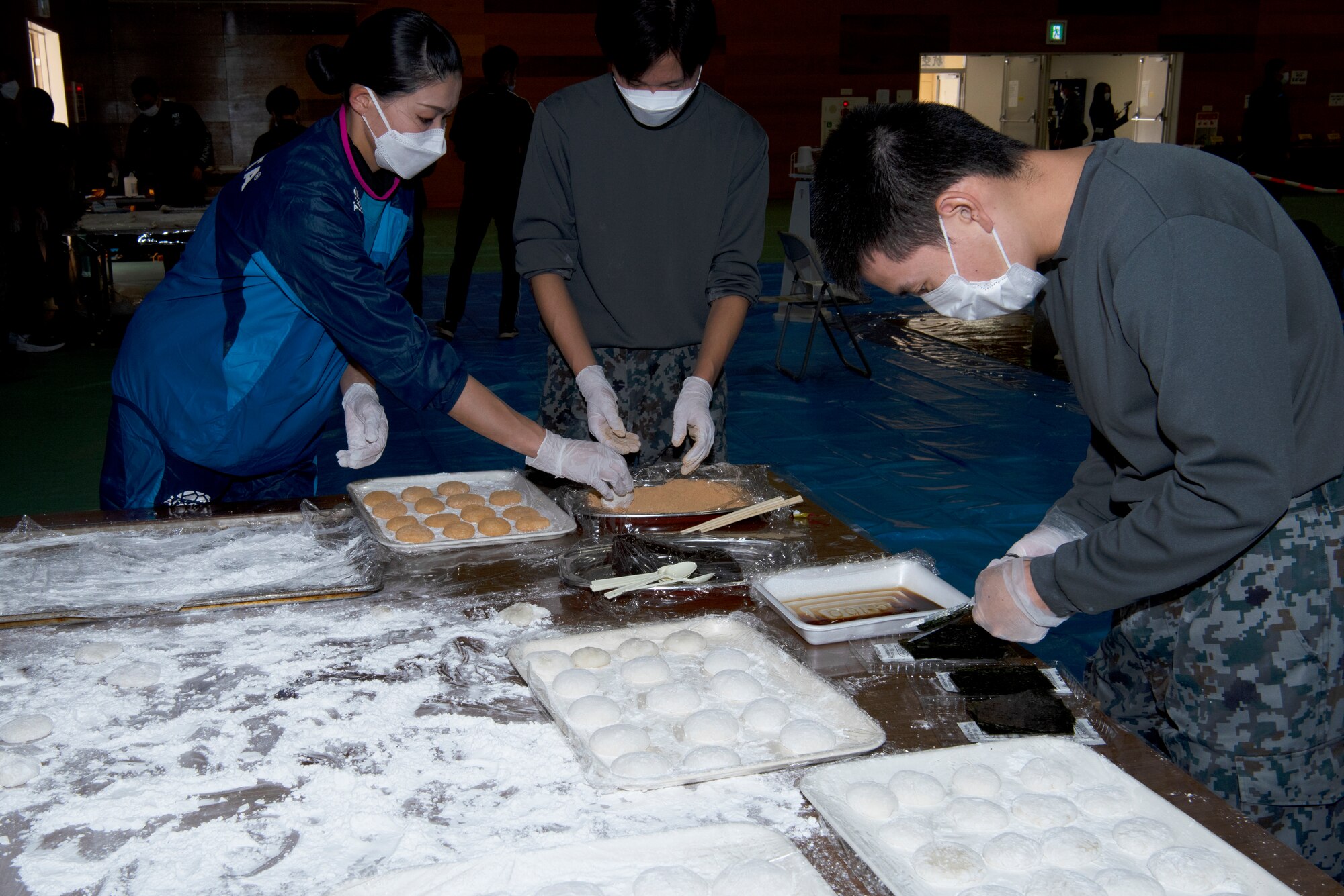 A team of volunteers dip freshly pounded rice dough into a peanut powder coating at the Operation Support Wing annual mochi pounding ceremony on Dec. 14, 2022, Yokota Air Base, Japan. Mochi is a traditional Japanese rice cake that is made just in time for the New Year and is widely considered a symbol for health and prosperity. The rice was pounded until it became a firm gelatin-like substance that was ripped apart and shaped into snack-sized treats by hand. (U.S. Air Force photo by Tech Sgt. Taylor A. Workman)