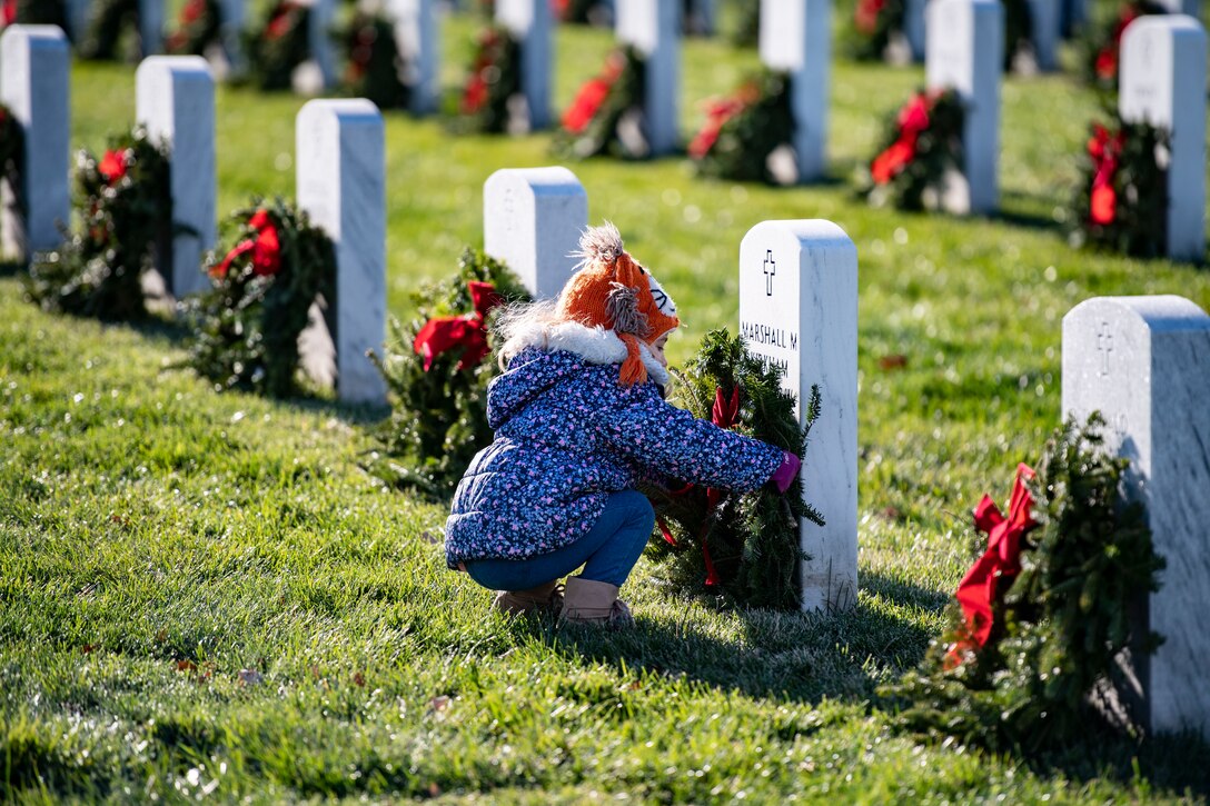 A young girl places a wreath on a headstone.