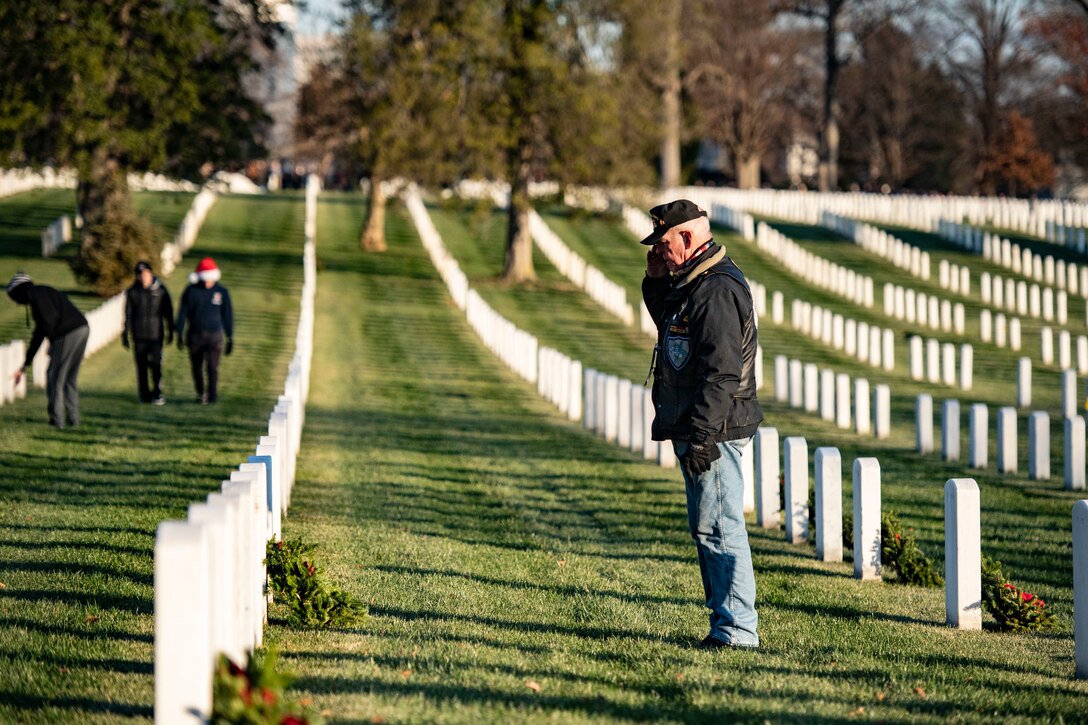 A man salutes in front of a headstone.