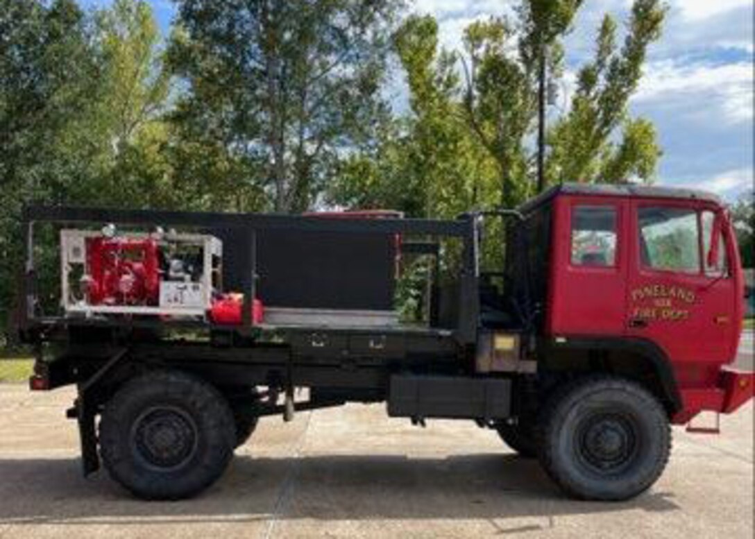 The former military truck converted to a firetruck sits outside showing off it's new coat of red paint and pump and tank set up on it flat bed.