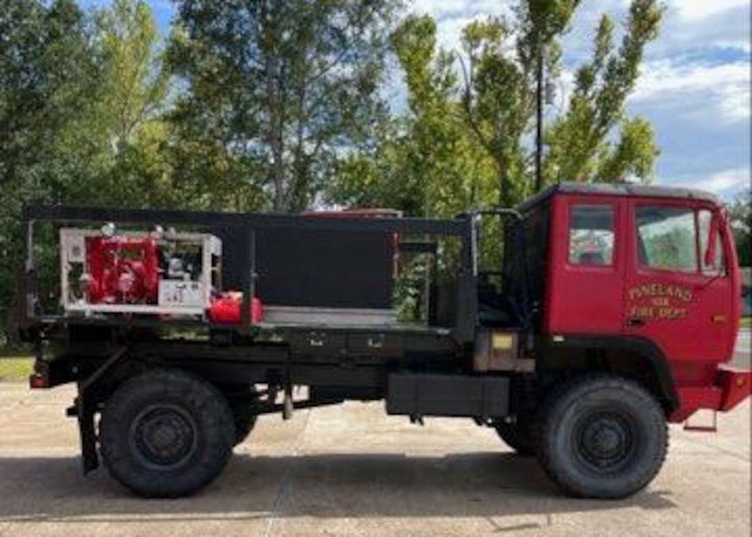 The former military truck converted to a firetruck sits outside showing off it's new coat of red paint and pump and tank set up on it flat bed.