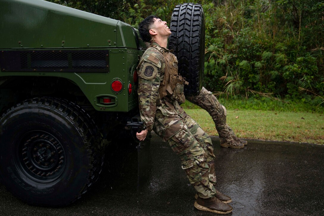 Two airmen push a vehicle in the rain near trees.