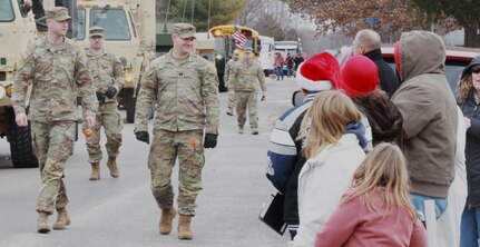 Maj. Christopher Hanson, left, the operations officer of the 232nd Combat Sustainment Support Battalion, and Capt. Jacob Brue, the battalion's training officer, carry flowers for June Peden-Stade along her parade route in Auburn, Illinois, Dec. 17, 2022. The Illinois National Guard joined hundreds of first responders and community groups from across the region to give 3-year-old June a parade.