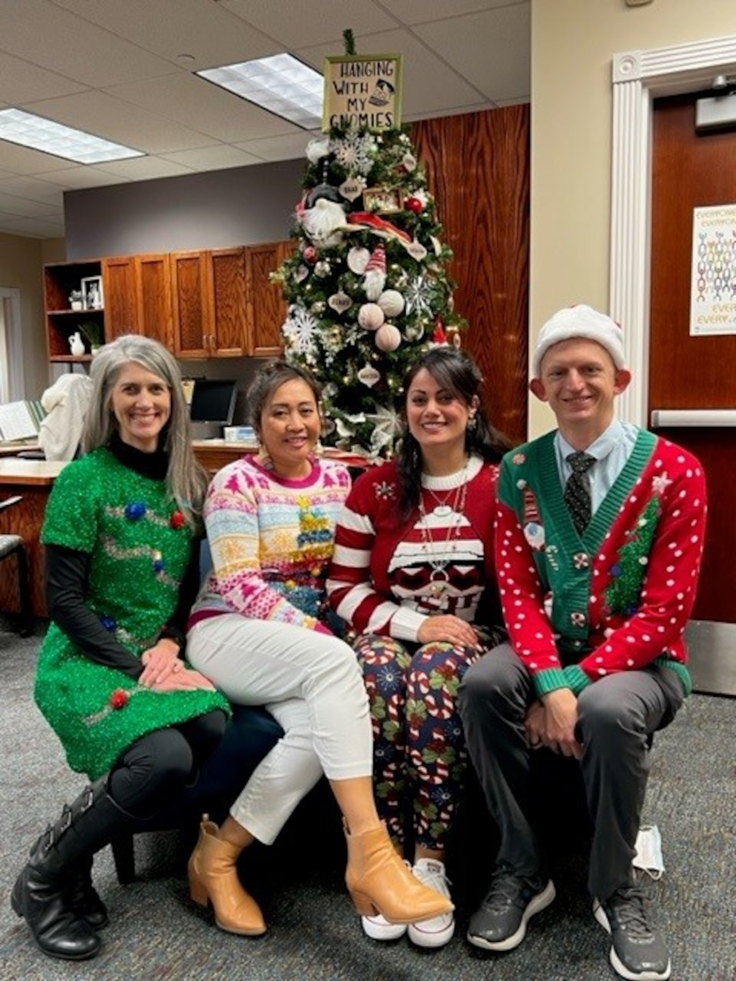 Three ladies and a man dresser in holiday garb sit on a bench in an office