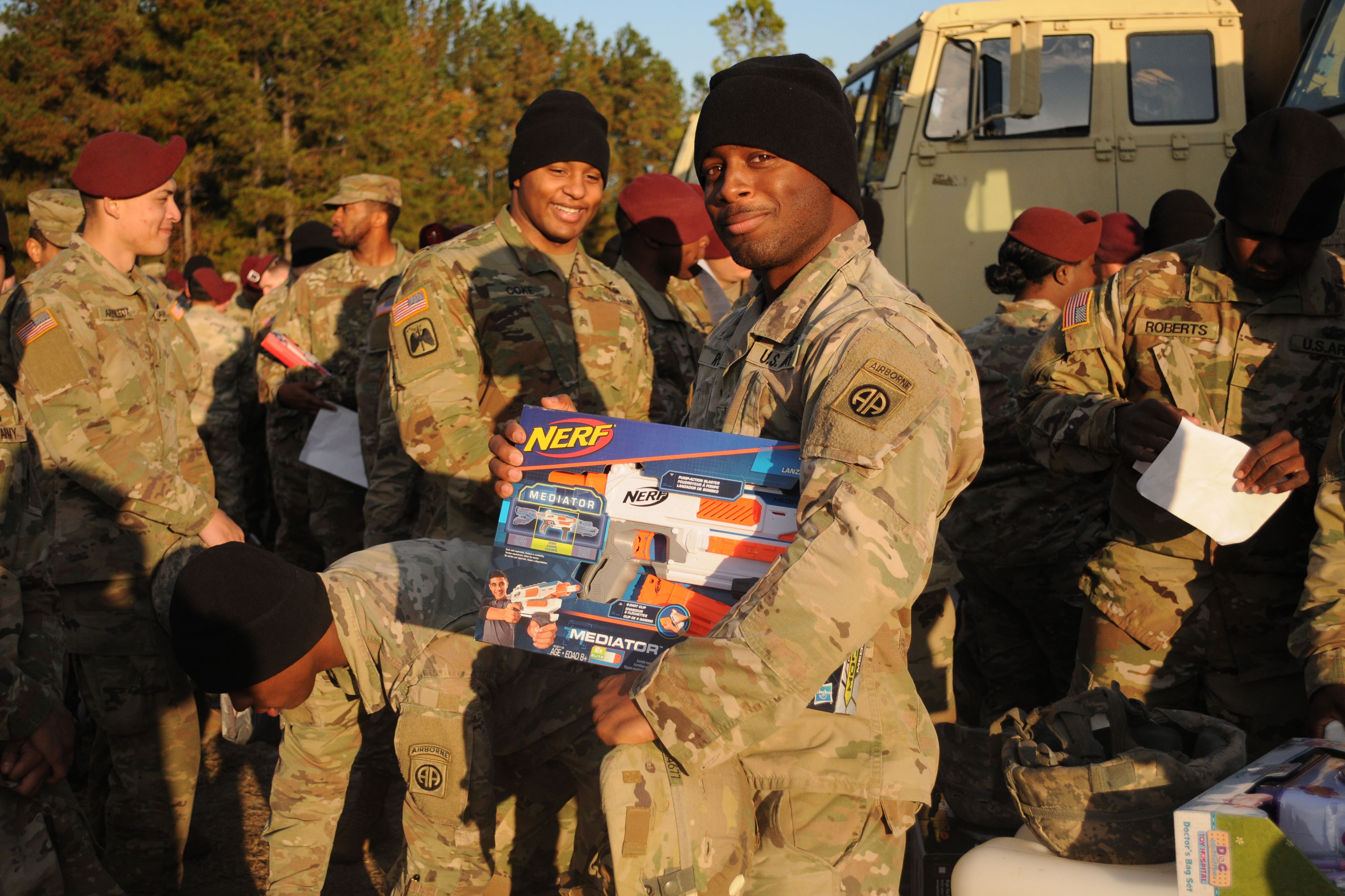 Soldiers holding gifts stand in a line as one smiles at the camera.