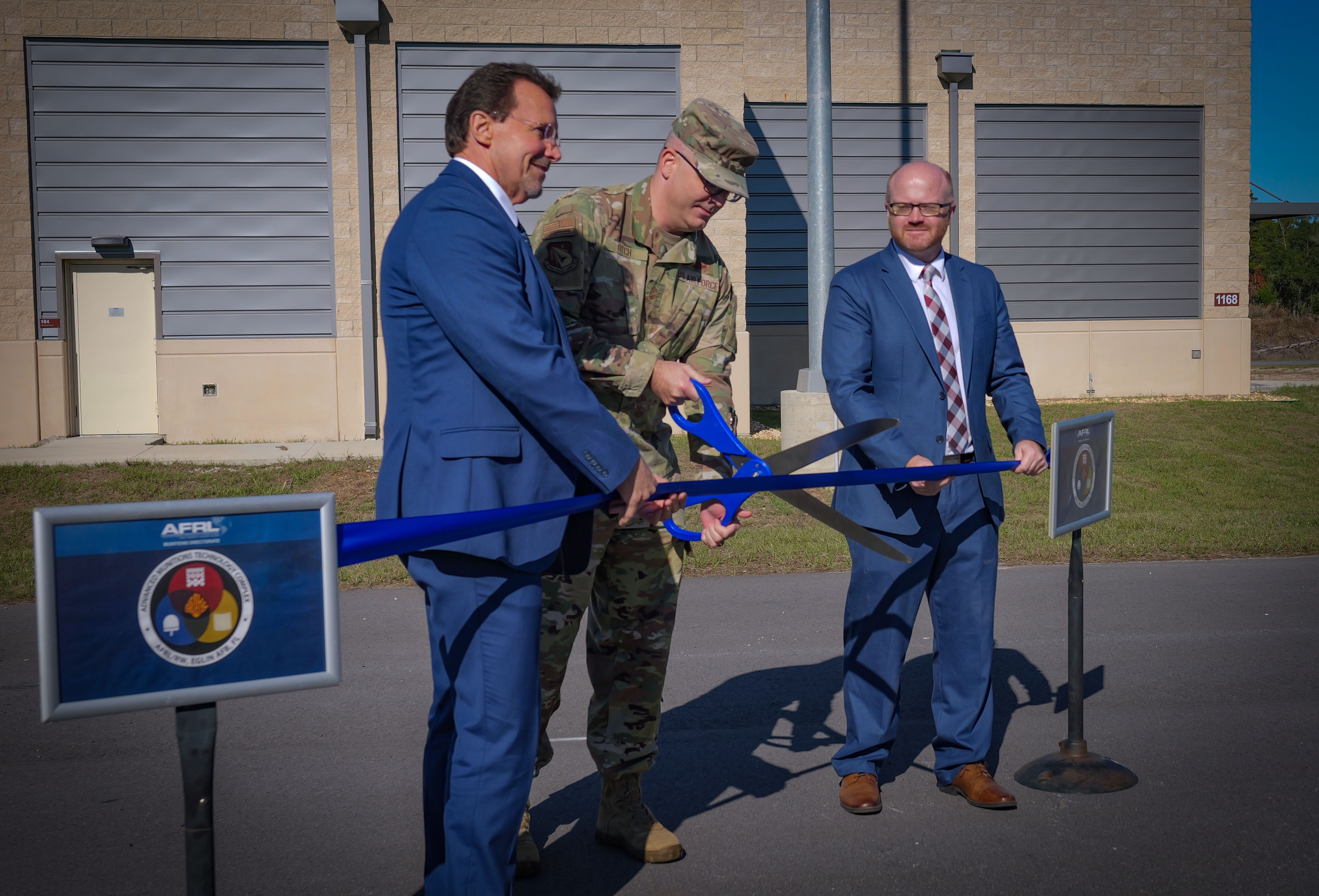Dr. David Lambert, left, chief scientist, AFRL’s Munitions Directorate; and Dr. J. Jacob Morris, right, chief, Energetics Materials Branch, ordnance division at AFRL’s Munitions Directorate, assist Chief Master Sgt. James “Bill” Fitch, AFRL Command Chief, in a ribbon-cutting ceremony for the lab’s newly constructed Advanced Munitions Technology Complex, or AMTC, at Eglin Air Force Base, Florida, Dec. 15, 2022. This military construction project, worth approximately $165 million, provides new test capability and modernizes much of the outdated 1960s infrastructure. AFRL designed the AMTC as a modern, collaborative research space that gives scientists and engineers the ability to experiment with new explosive materials and integrate them into complex munition designs. (U.S. Air Force photo / Keith Lewis)