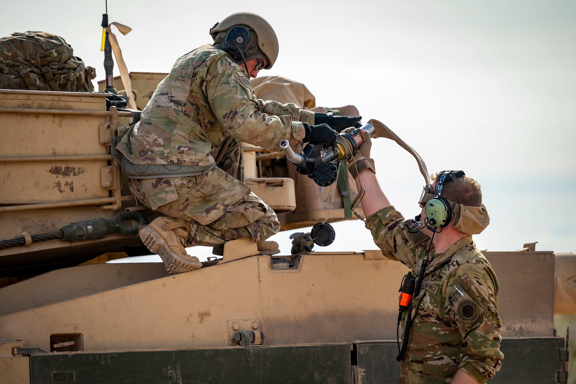 A U.S. Army member assigned to the 1st Armored Division grabs a fuel pump from Tech. Sgt. Christopher Hofer, 40th Airlift Squadron weapons instructor, after simulating refueling a M1A2 Abrams tank from a C-130J Super Hercules at Fort Bliss, Texas, Dec. 9, 2022. This exercise allowed aircrew with the C-130J to refuel Army ground vehicles enabling expeditious and mobile logistics for Army ground forces. (U.S. Air Force photo by Senior Airman Leon Redfern)