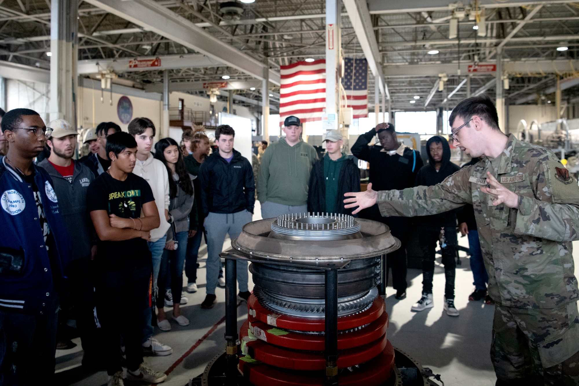 U.S. Air Force Senior Airman Nicholas Shaw, 20th Component Maintenance Squadron F110 Jet Engine Intermediate Maintenance technician, shows Florence 1 School District’s Advantage Academy students parts of an engine used in F-16 Fighting Falcon operations at Shaw Air Force Base, S.C., Nov. 30, 2022. Units from Ninth Air Force (Air Forces Central), 15th Air Force and the 20th Fighter Wing worked together to host an engagement for 35 local high school students as part of Project Quesada. The new Air Combat Command-led program is designed to attract and recruit talented students seeking careers in aviation, science, technology, engineering and math in an effort to develop future aviators and leaders. (U.S. Air Force photo by Staff Sgt. Kelsey Owen)