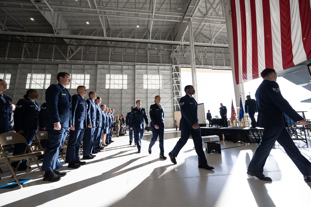 Airmen in formal uniforms walk in a line toward a stage.