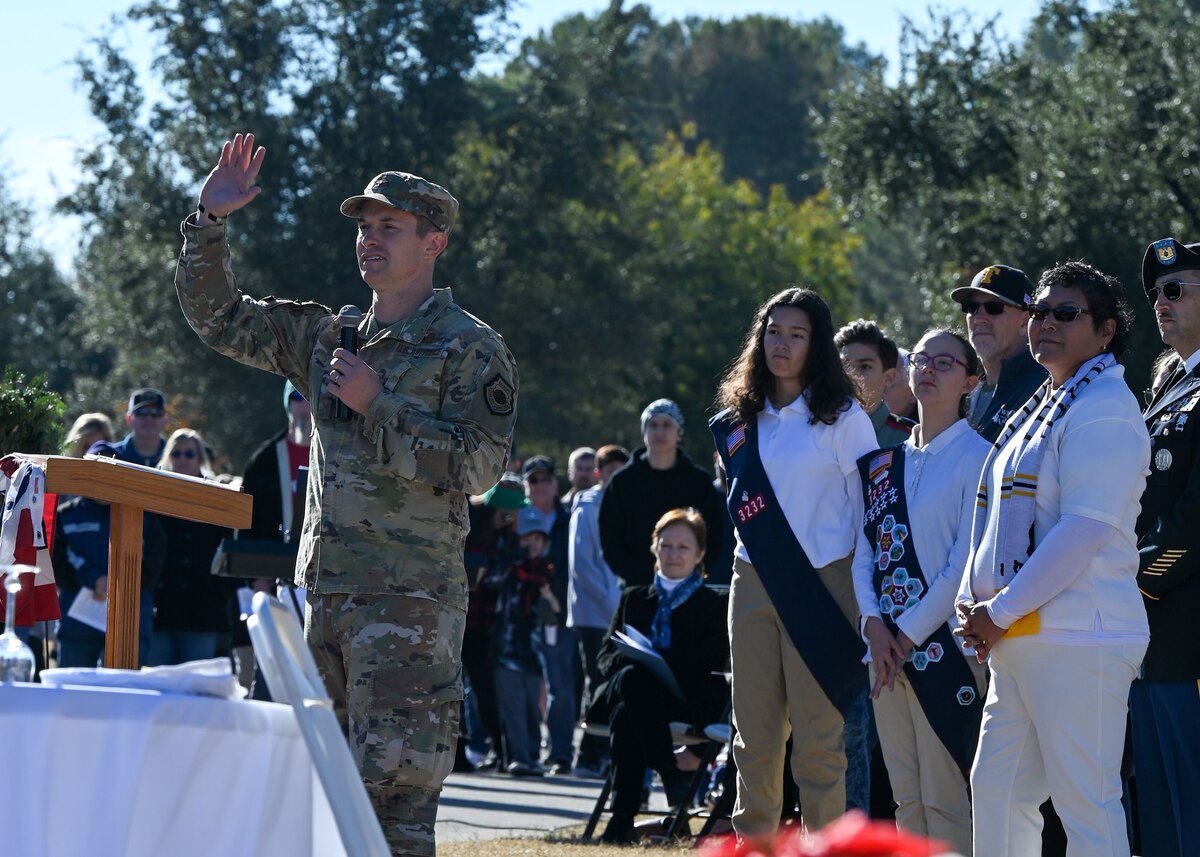 A man in a military uniform waves to a crowd while he speaks to them.