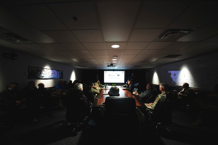 Personnel sit around a table in front of a presentation.