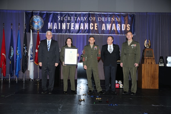 Marines from Exercise Support Division, Marine Corps Air Ground Task Force Training Command, Marine Corps Air Ground Combat Center, Twenty-nine Palms, Calif., are presented with the Secretary of Defense Small Field-Level Maintenance Unit Award for FY21 by the Honorable Christopher J. Lowman, far left, Assistant Secretary of Defense for Sustainment, during an awards banquet held at the Department of Defense Maintenance Symposium in Orlando, Fla., Dec. 13.