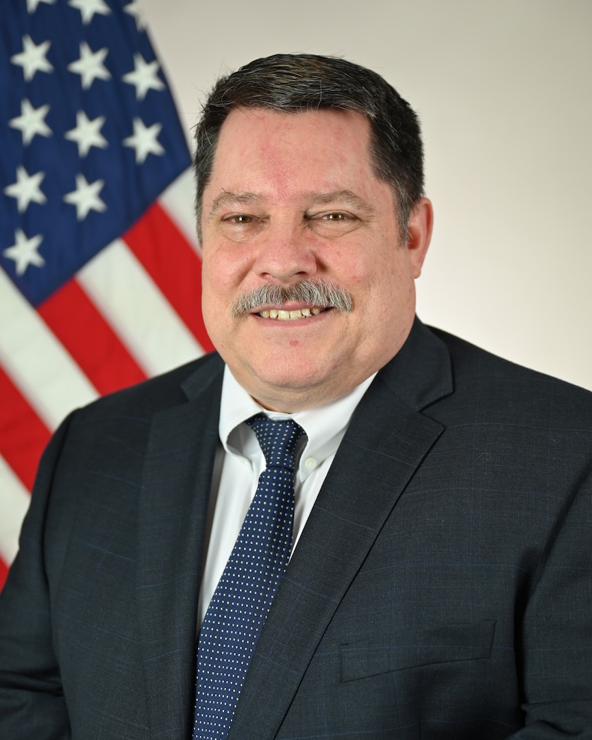 The official photo for Ronald Buonanducci. He is wearing a dark suit and tie and is seated for a photo in front of an American flag.
