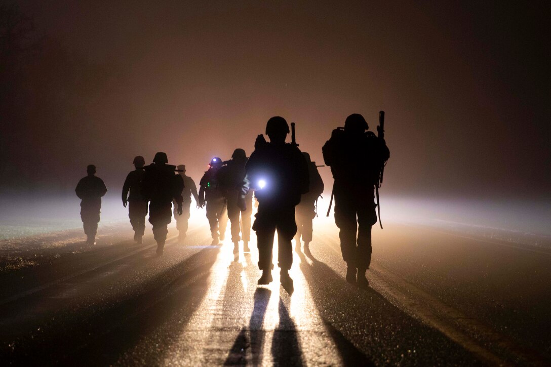 A group of soldiers walk together in the dark carrying flashlights.