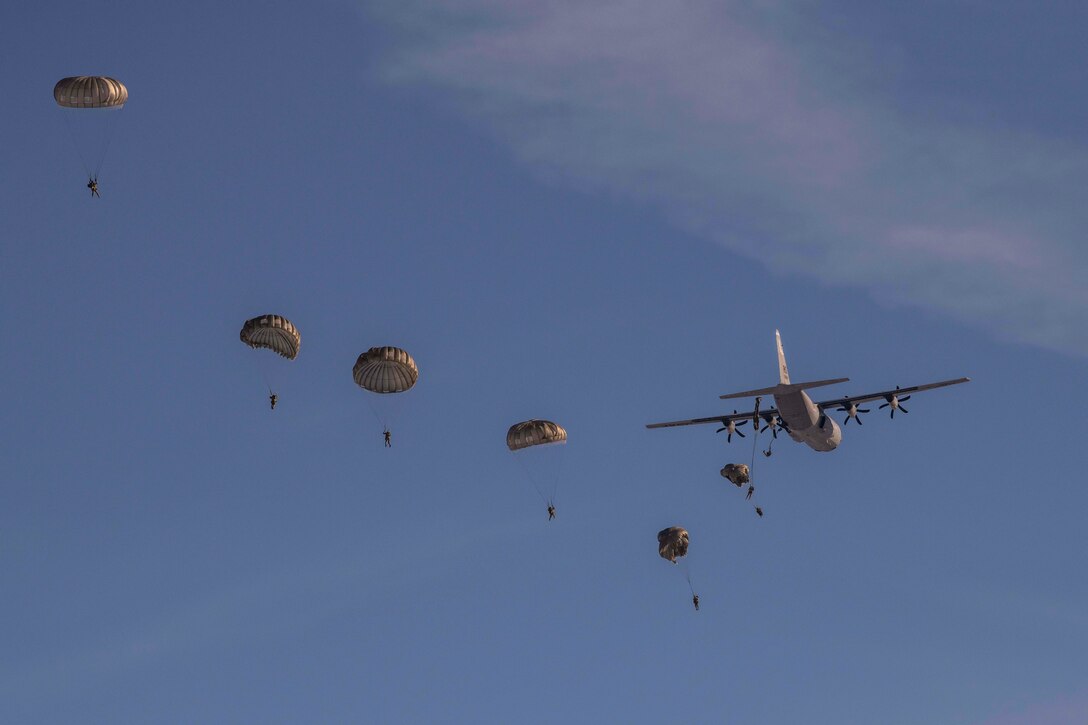 Soldiers jump from an aircraft and free fall with parachutes.