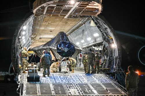 Airmen attach a hitch to the front wheel of an F-22 Raptor fuselage inside a C-5M Galaxy