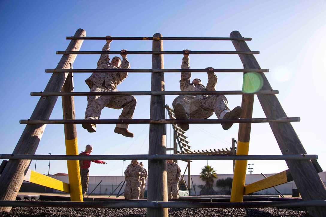 Two Marine Corps recruits climb an obstacle.