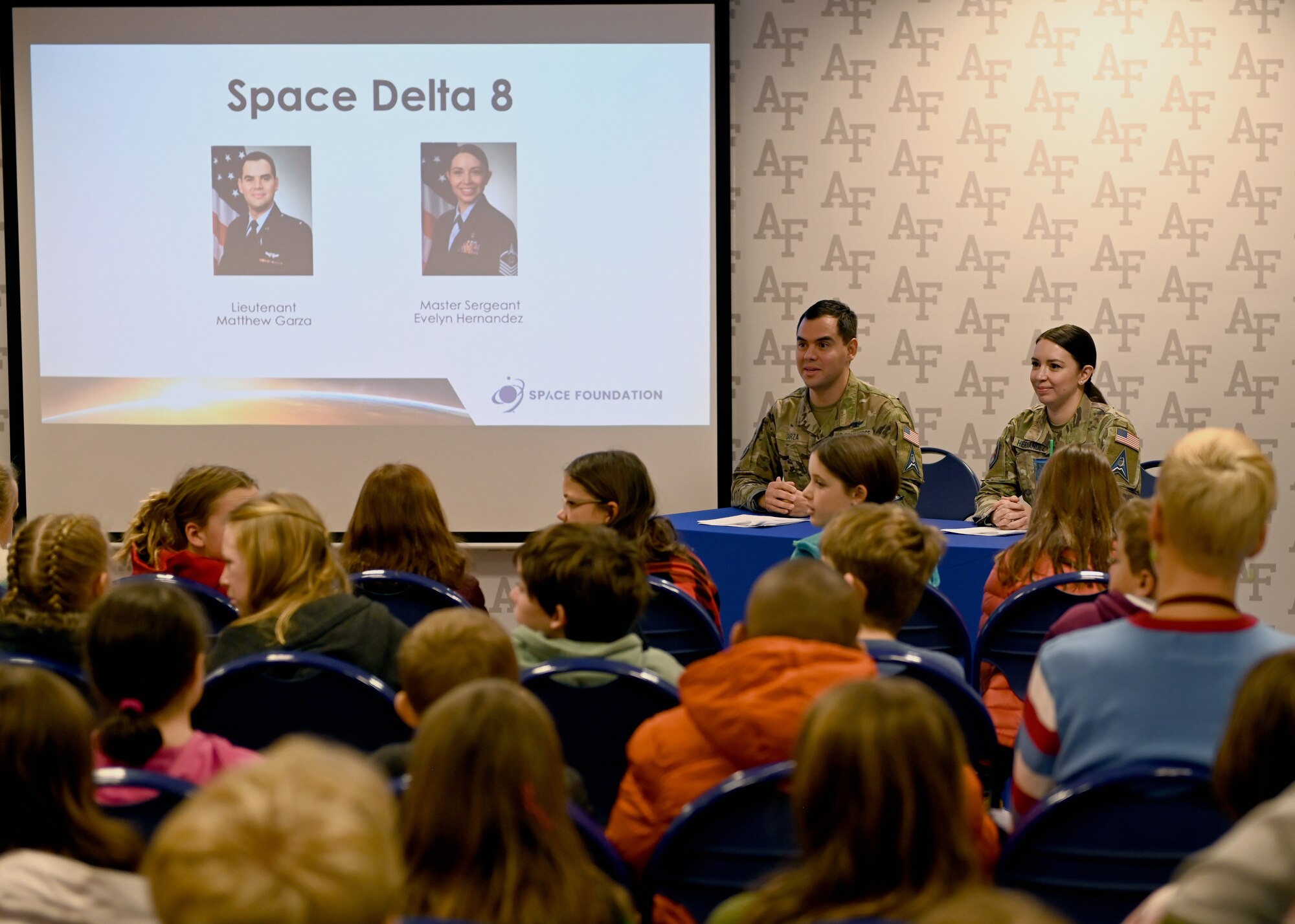 Two Space Force Guardians at a table answering questions to a group of elementary school students during a STEM-to-Space event at the Air Force Academy in Colorado, December 15, 2022.