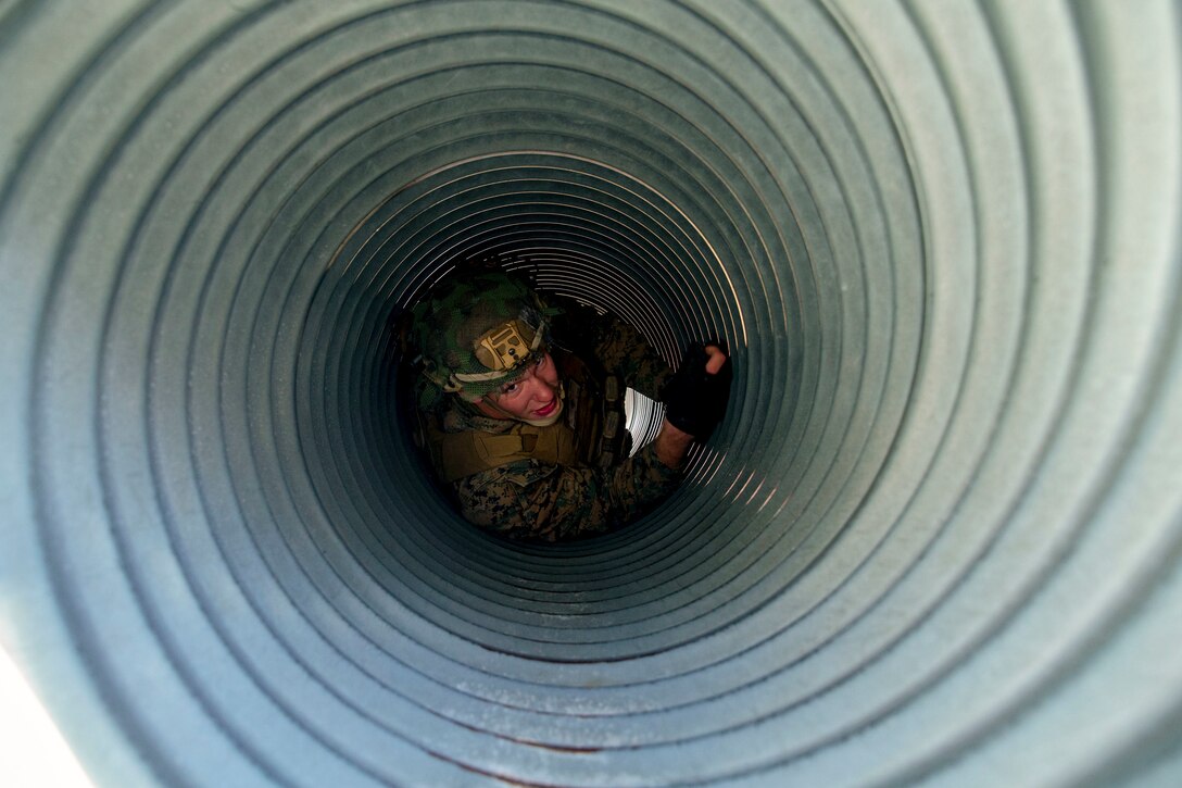 A Marine crawls through a ridged metallic tunnel.