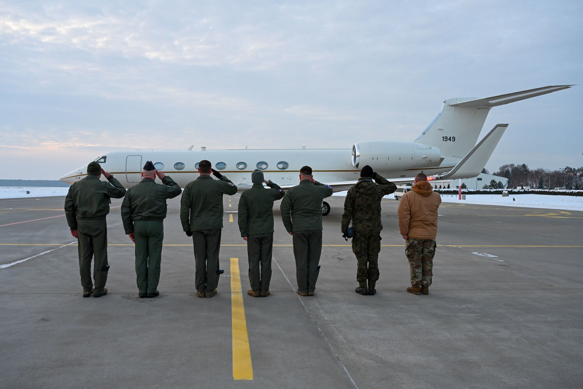Military members salute in front of aircraft