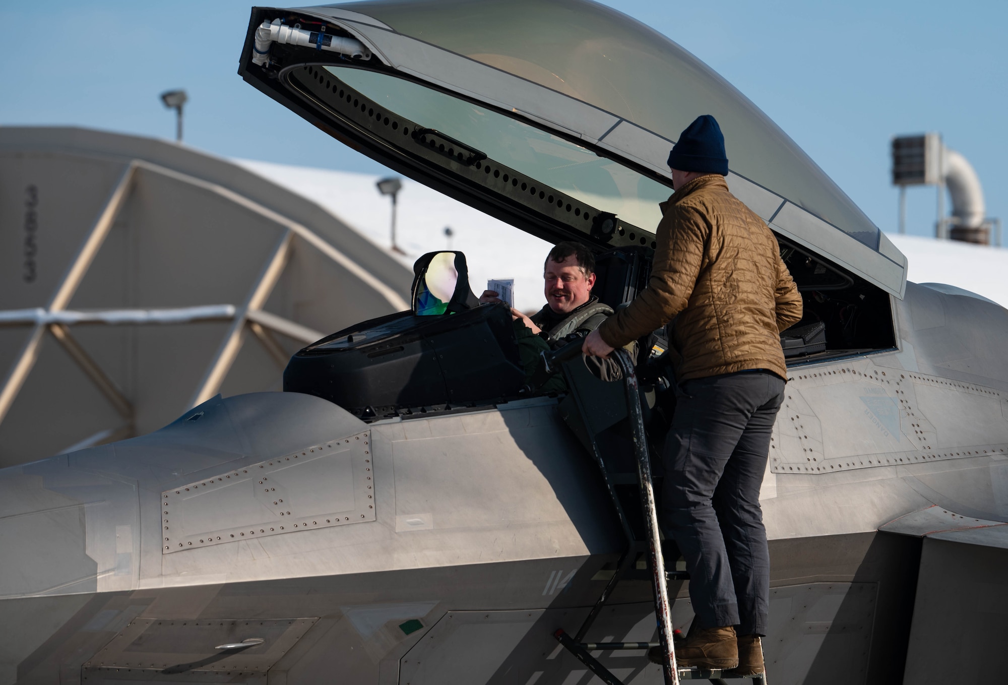 Pilot greets Airman in cockpit of F-22.