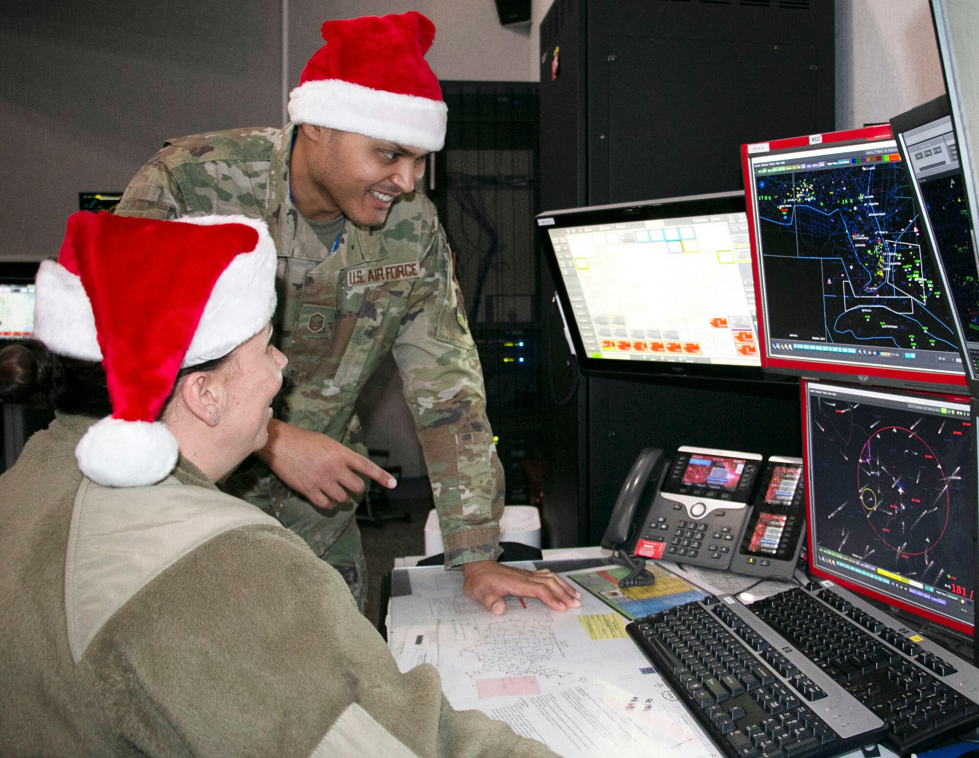 Air Force Master Sgt. Brian Burgess, standing, and Maj. Bonnie Bosworth of the New York Air National Guard’s 224th Air Defense Squadron train for Santa tracking operations on Dec. 16, 2022, at Eastern Air Defense Sector headquarters  in Rome, N.Y.