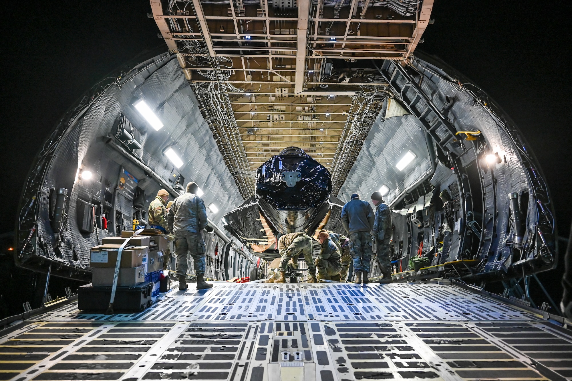 Airmen attach a hitch to the front wheel of an F-22 Raptor fuselage inside a C-5M Galaxy