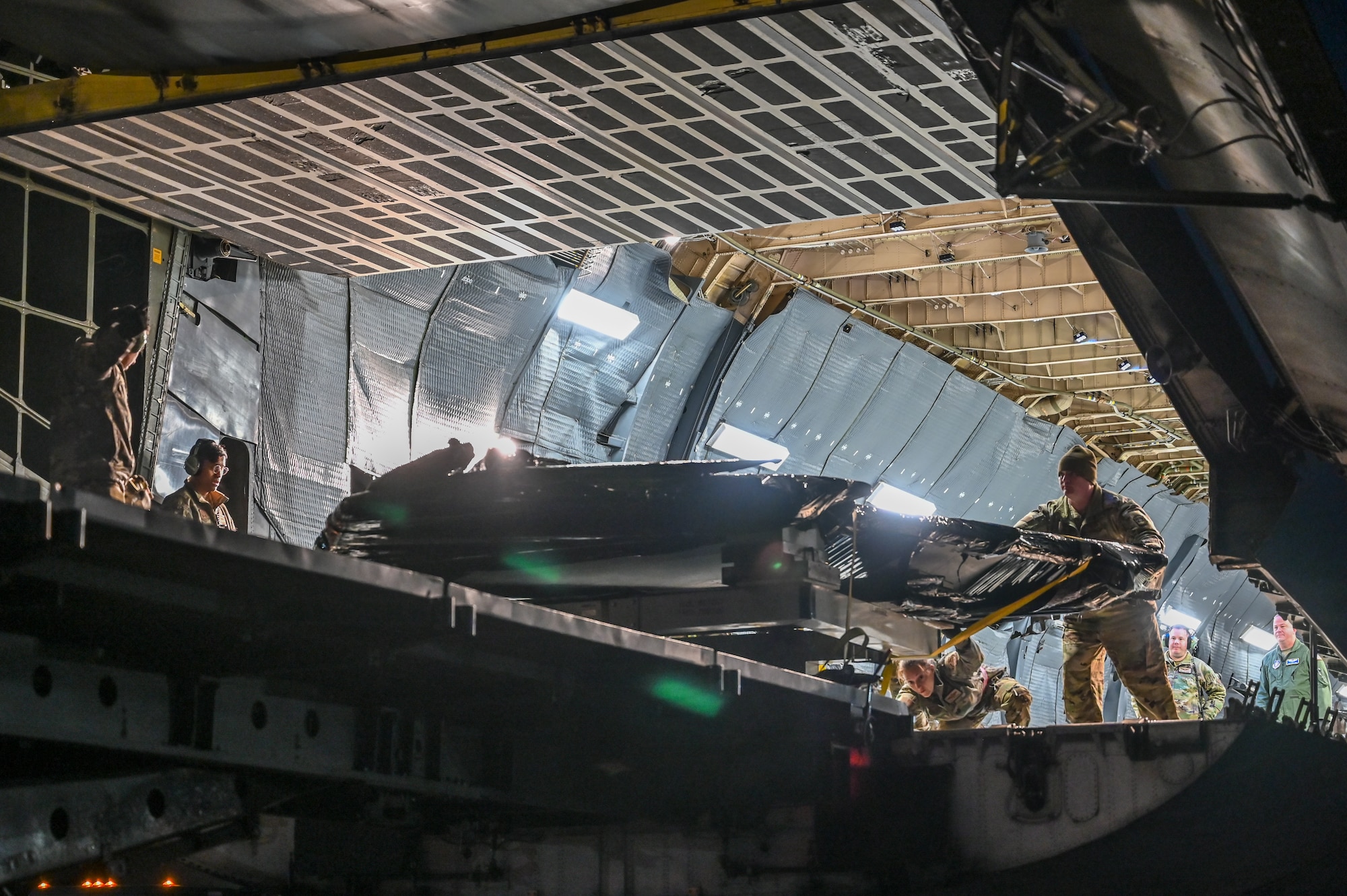 Airmen push the wings of an F-22 Raptor from inside a C-5M Galaxy