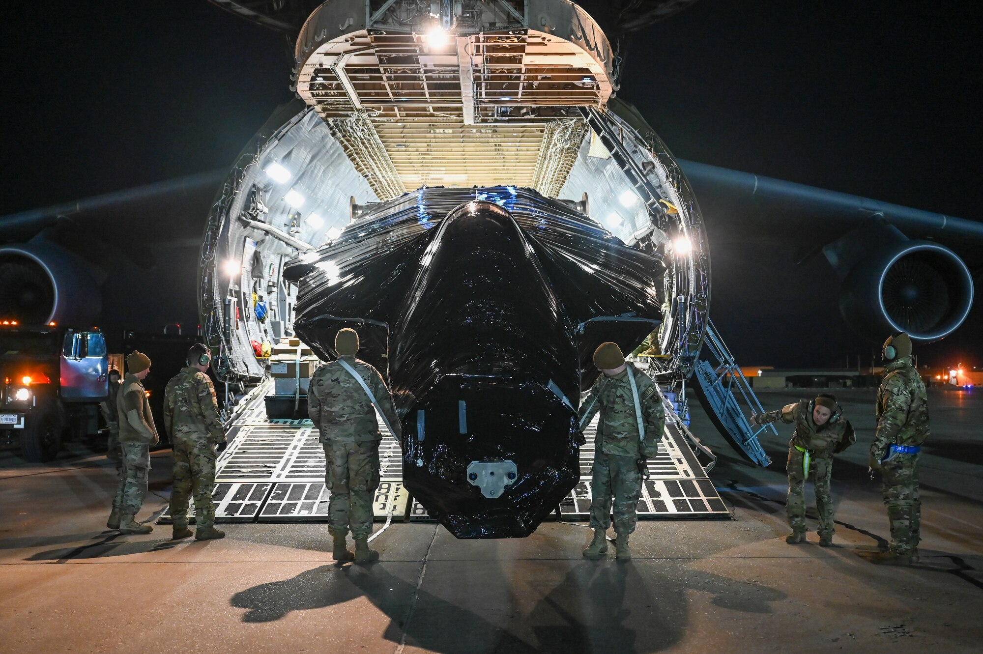 Airmen pull the fuselage of an F-22 Raptor from inside a C-5M Galaxy