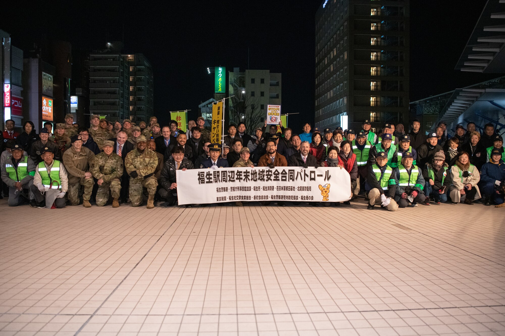 Yokota Air Base leadership and community members pose for a group photo while holding a banner