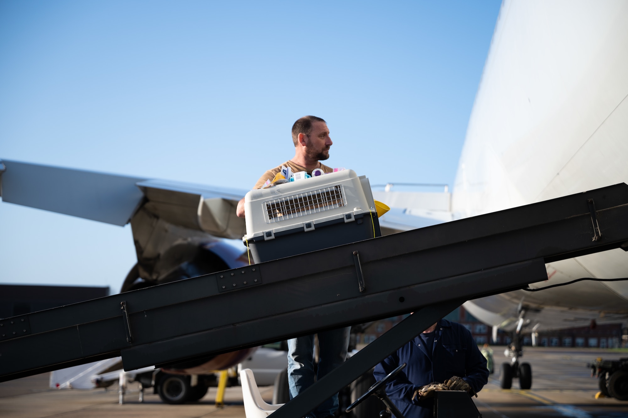 A U.S. Air Force fleet service contractor guides a pet carrier onto the Patriot Express, atRoyal Air Force Mildenhall, Dec. 20, 2022. The Patriot Express flight, also known as the rotator, helps alleviate the stress of members permanently changing station to the United Kingdom with pets by allowing for 10 pets in-cabin and 10 pets in the aircraft belly. (U.S. Air Force photo by Airman 1st Class Viviam Chiu)