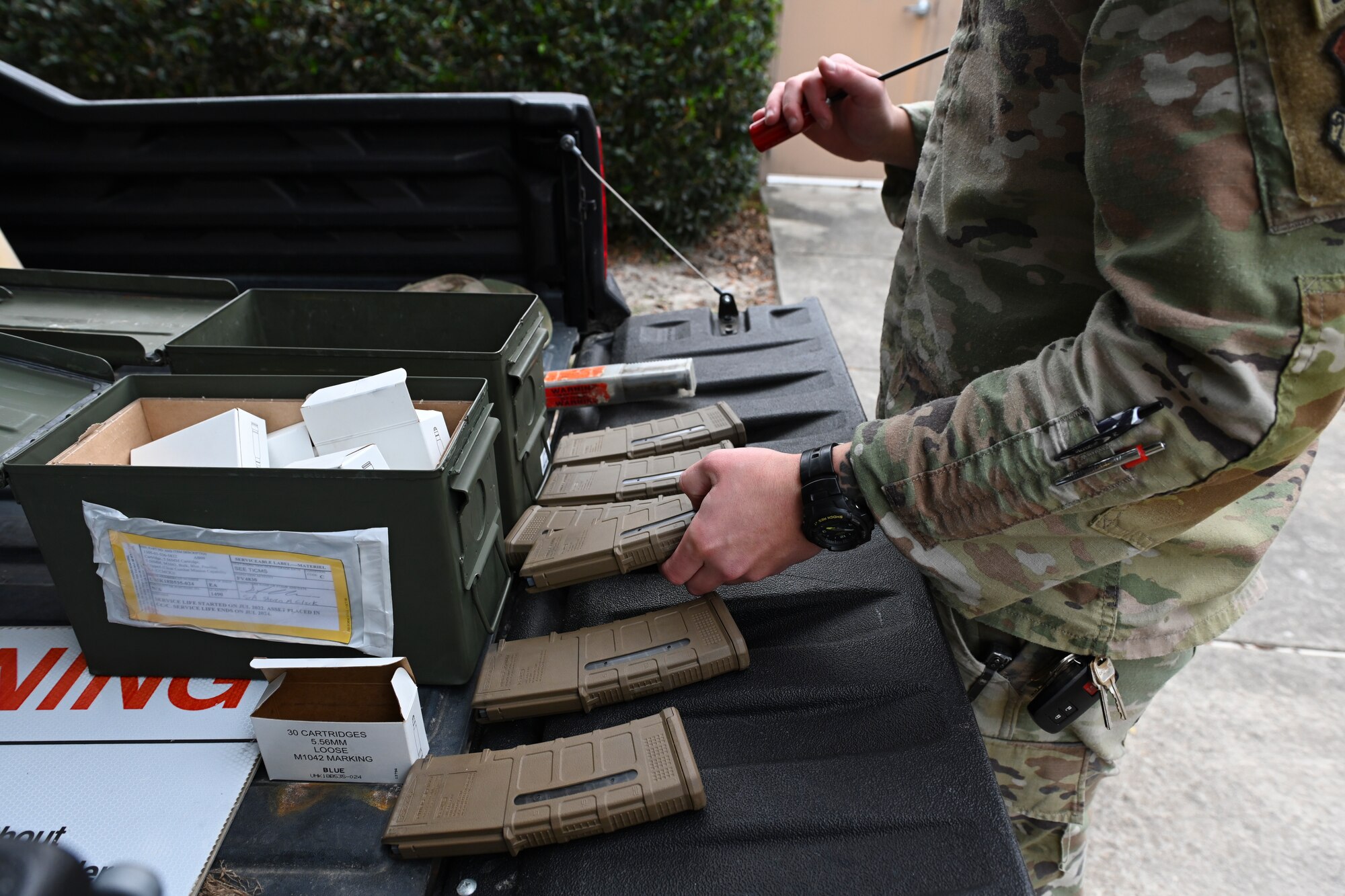 A photo of someone placing an M-4 magazine in a row with 5 other magazines in the back of a black ATV trunk.