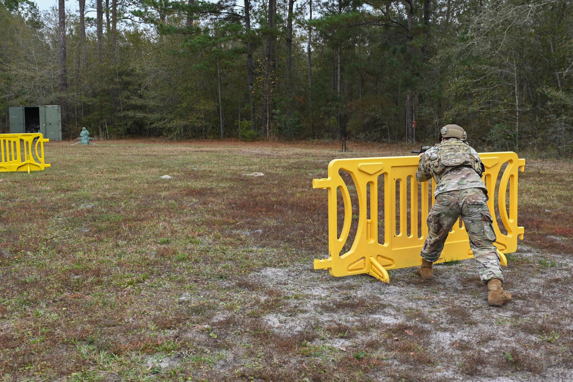 A photo of an Airman standing behind a yellow barrier, aiming his weapon at a green human-like dummy.