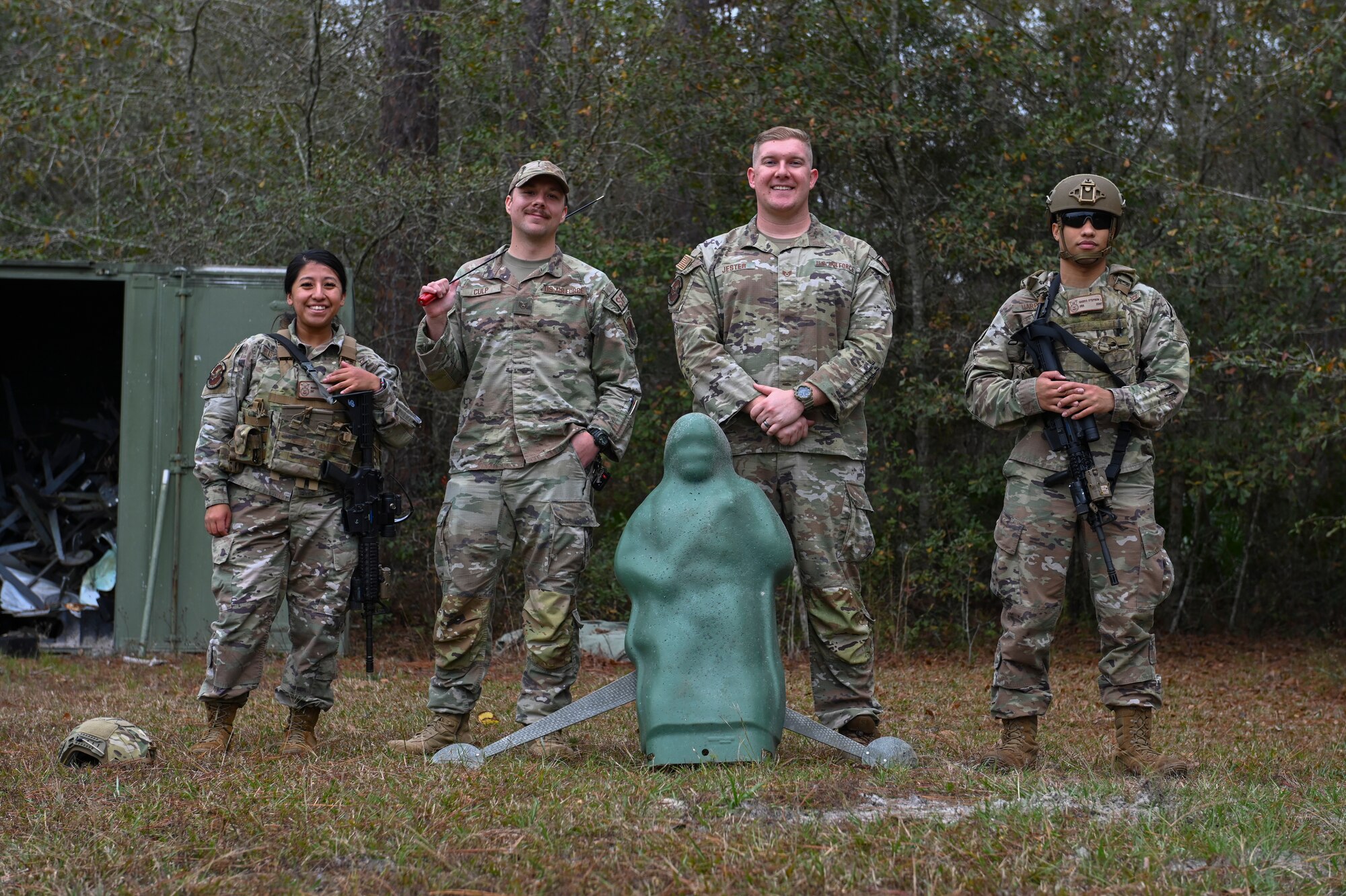 A photo of four Airmen standing in a row in front of a green human-like target used for training.