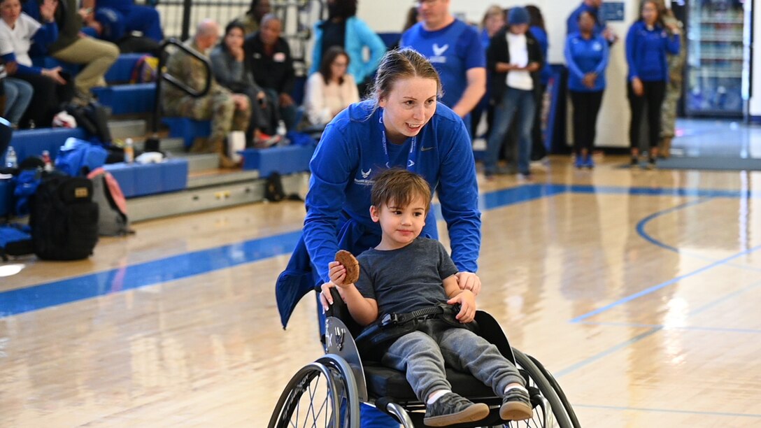 A woman pushes her young son in a wheelchair basketball chair.