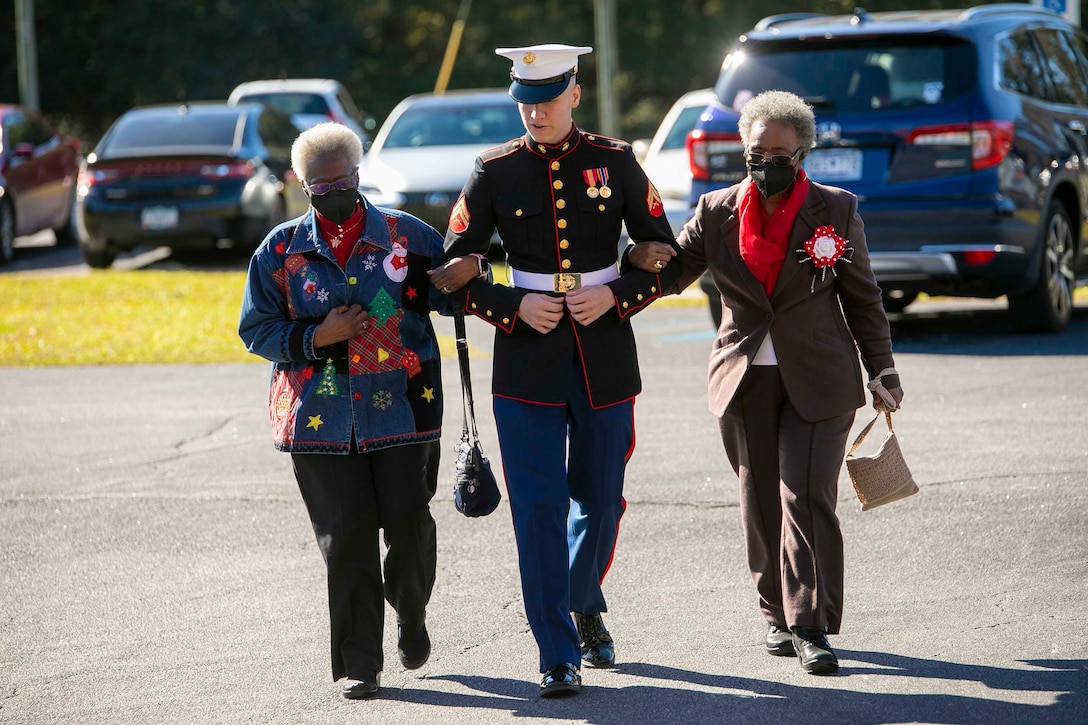 A Marine escorts two women through a parking lot.