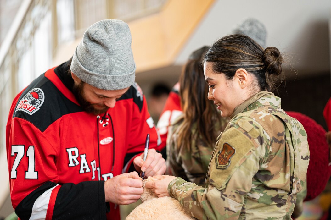 Jon Martin, Rapid City Rush Hockey Team player, signs a teddy bear for Airman 1st Class Sharon Plascencia Mendoza, 28th Bomb Wing Judge Advocate Office military justice paralegal, at Ellsworth Air Force Base, South Dakota, Dec. 21, 2022. Members of the Rapid City Rush Hockey Team and Black Hills Energy donated 250 teddy bears for military families who currently have a family member deployed. (U.S. Air Force photo by Staff Sgt. Alexi Bosarge)