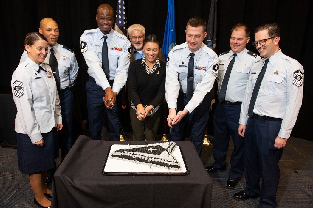 Group of Space Force Guardians stand around a cake. Three have swords and are cutting the cake.