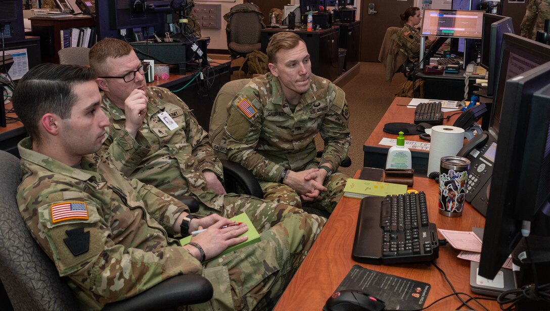 Pennsylvania National Guard Joint Operations Center operations noncommissioned officers Sgt. John Marru, Staff Sgt. James R. Ergott, and Sgt. Christopher R. Galbraith participate in a winter storm tabletop exercise from the JOC floor Dec. 20, 2022, at Fort Indiantown Gap, Pa. The exercise designed to improve and validate domestic response procedures. (Pennsylvania National Guard photo by Wayne V. Hall) (This photo was altered to obscure an ID card)