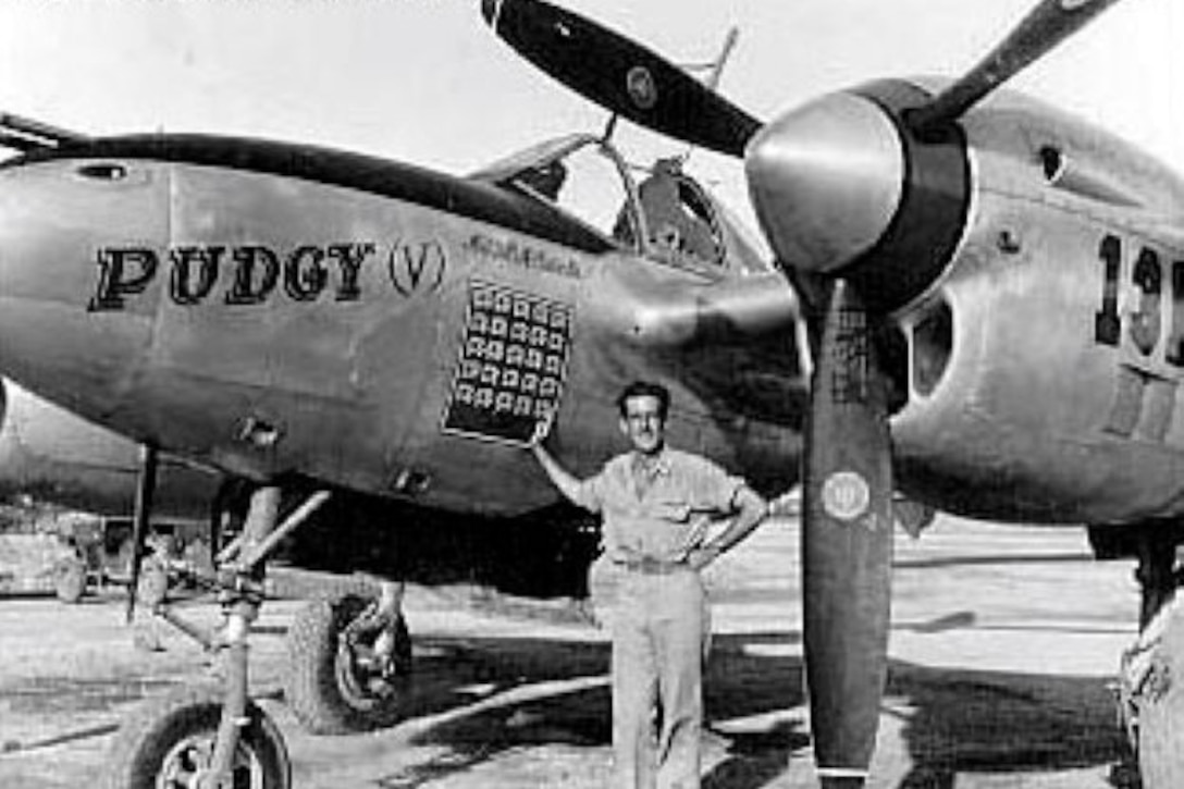 A man stands beside a propeller airplane.