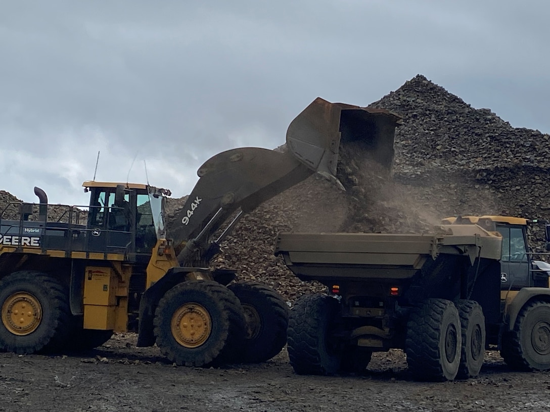Photo of a front loader construction truck dumping a load of rock onto a dump truck.