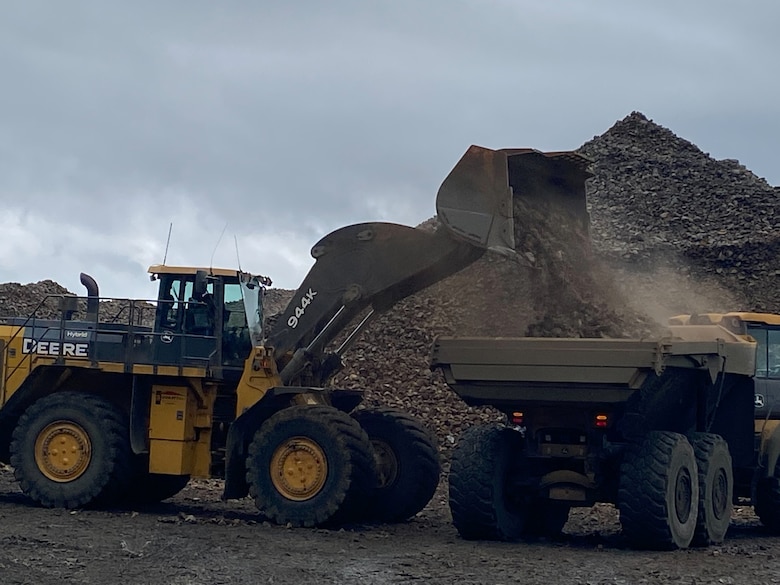 Photo of a front loader construction truck dumping its load of rock onto a dump truck,