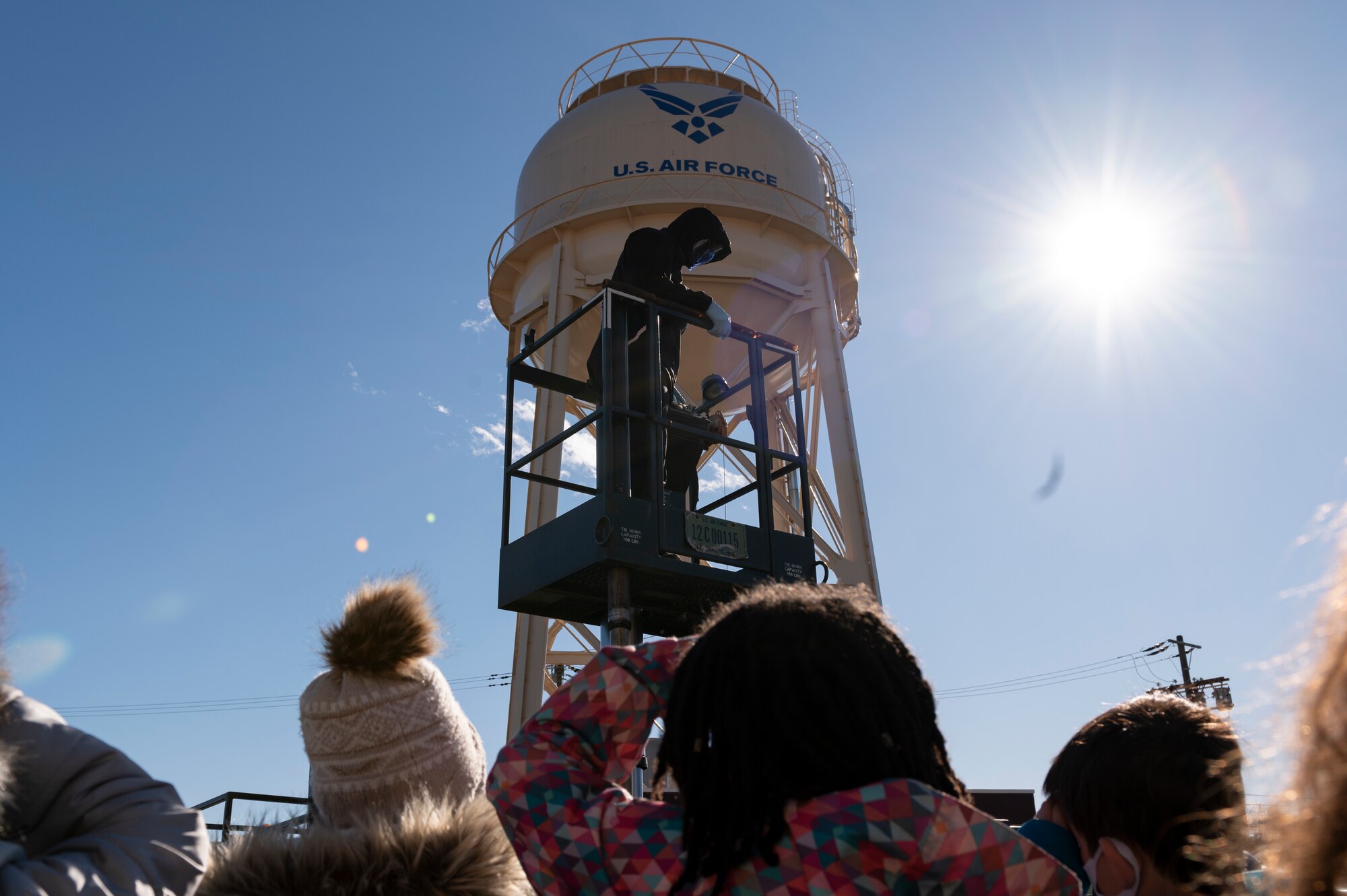 A tour guide stands on a lavatory truck lift in front of a water tower