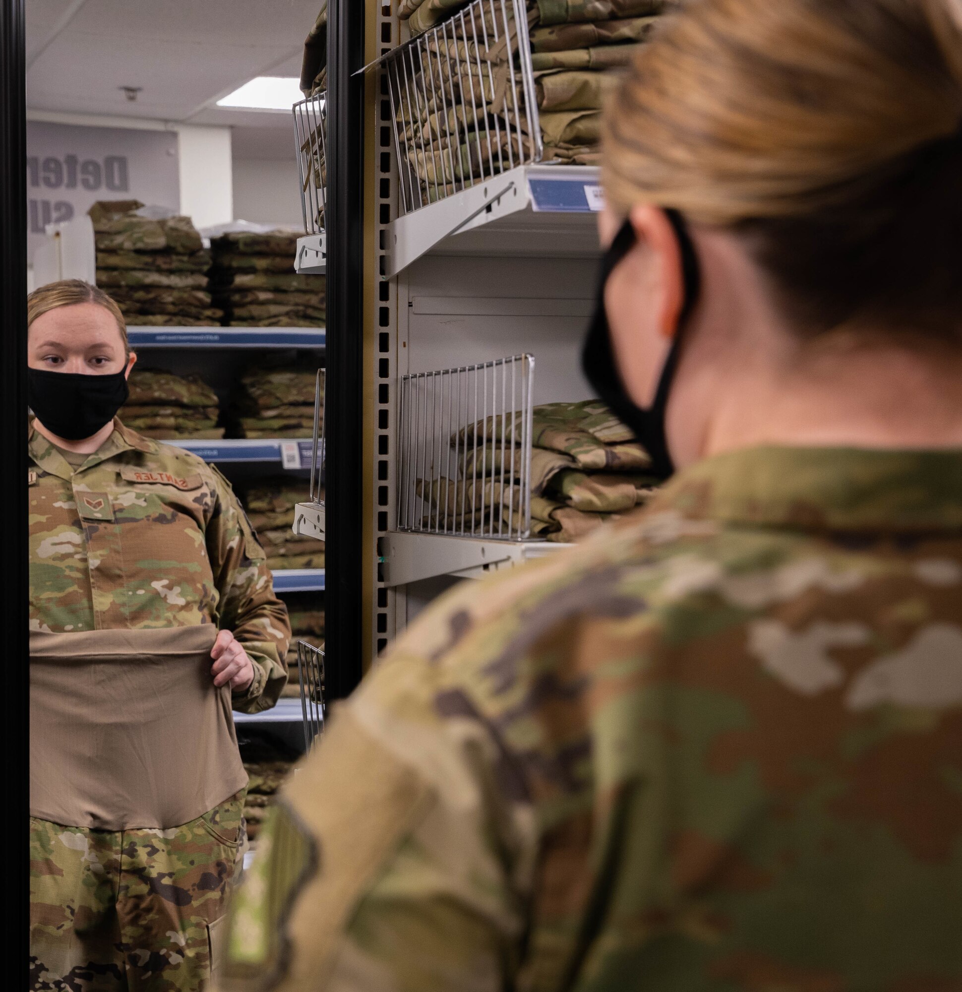Airman looks at herself in a mirror while holding maternity uniform pants to her waist