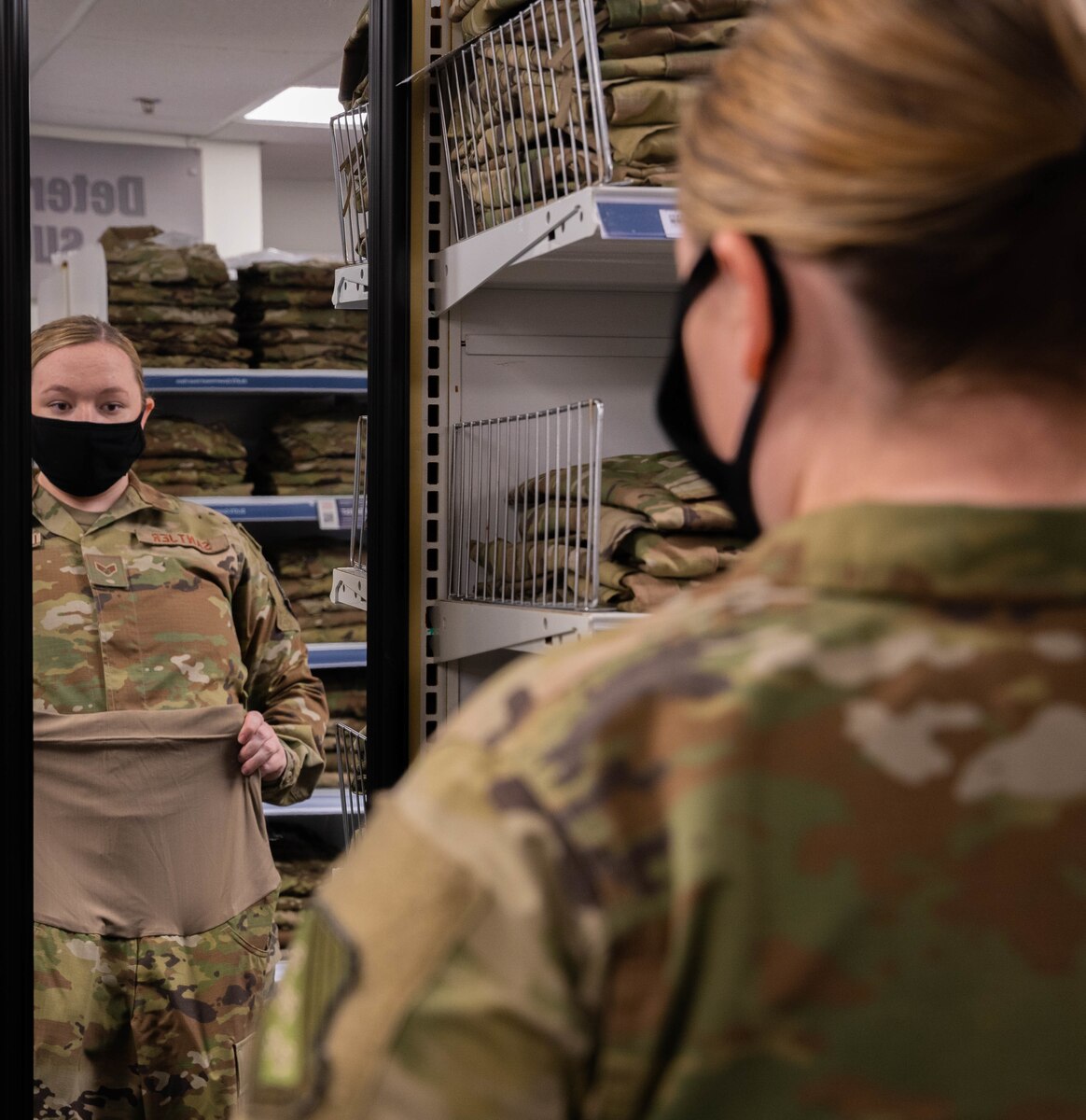 Airman looks at herself in a mirror while holding maternity uniform pants to her waist