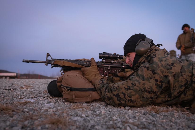 A man in military uniform aims a weapon.