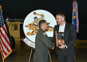 U.S. Air Force Lt. Col. Marcus Antonini, 325th Weapons Squadron commander, presents a commemorative plaque to Patrick McGeehan at Whiteman Air Force Base, Mo., Dec. 13, 2022. The plaque honors the legacy of McGeehan’s father Lt. Col. Mark McGeehan. (U.S. Air Force photo by Airman 1st Class Nash Truitt)