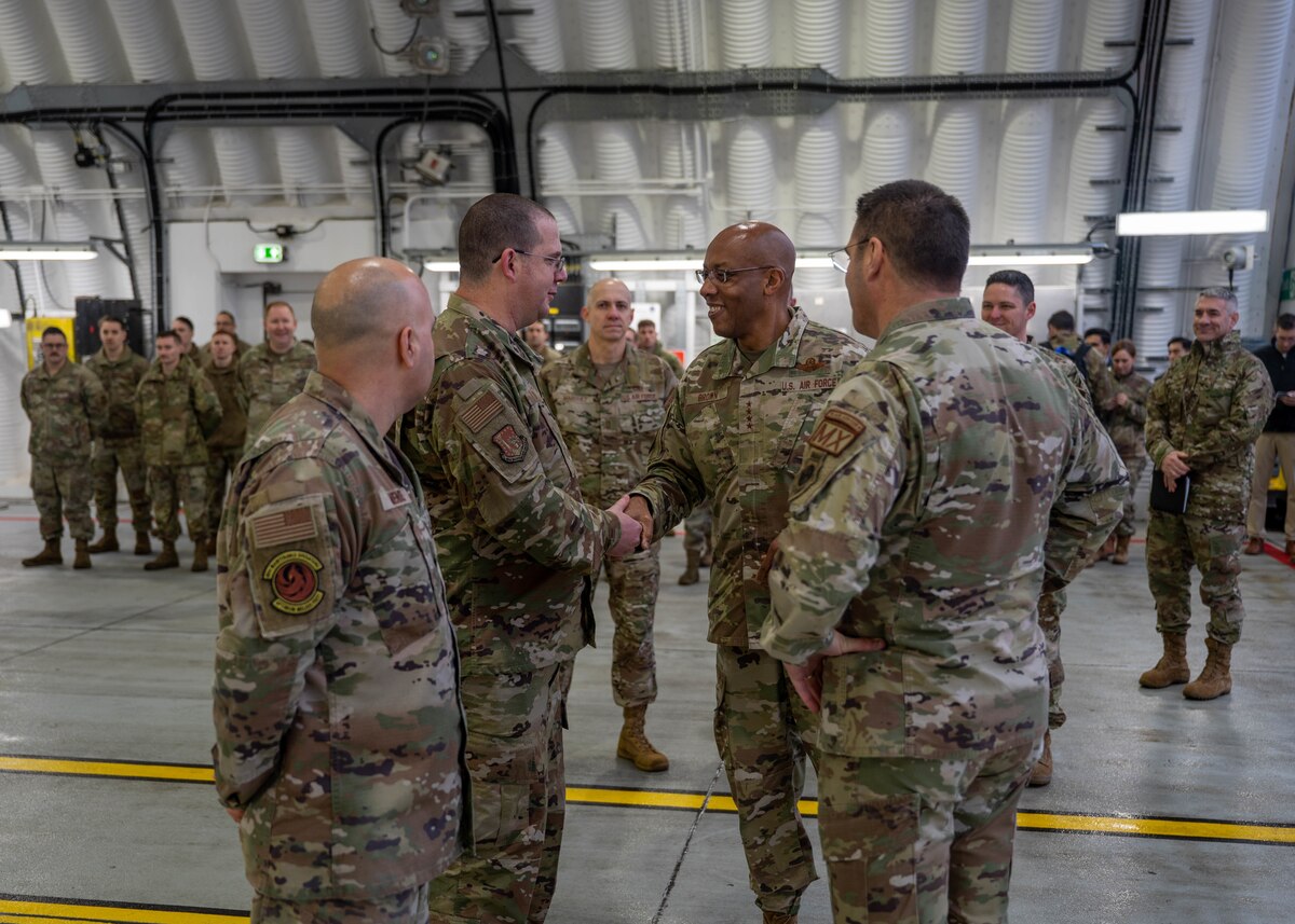 Two men shake hands in an aircraft hangar.
