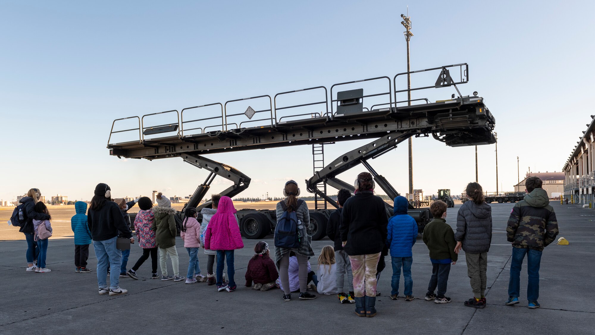 Assistants and children watch a tour guide showoff the features of a K-Loader cargo vehicle
