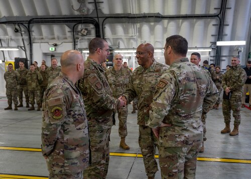 Two men shake hands in an aircraft hangar.